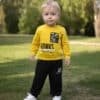 Sarı sweatshirt ve siyah pantolon giyen yürümeye başlayan çocuk.