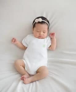 Beyaz tulumlu ve çiçekli taçlı uyuyan bebek.